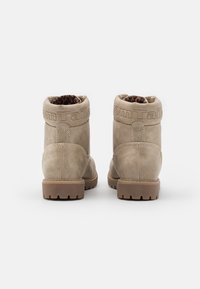 Bottines beige avec semelles robustes, couture visible, doublure en imprimé léopard, et nom de marque en relief sur le collier rembourré, vue de derrière.