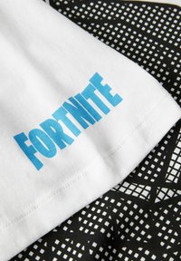 Bílá látka s modrým textem "FORTNITE", v kombinaci s černou látkou se mřížkovaným vzorem. Hladká textura, příležitostný design.