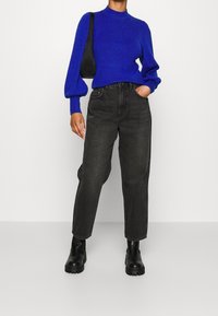 Pull blu royal con maniche a palloncino, abbinato a jeans grigi scuri a vita alta e stivali neri chunky alla caviglia. Borsa nera semplice.