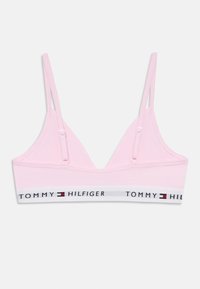 Jasnoróżowy biustonosz braletka z cienkimi, regulowanymi ramiączkami oraz białą elastyczną taśmą z logo "TOMMY HILFIGER" w granatowym i czerwonym kolorze. Gładka faktura materiału.