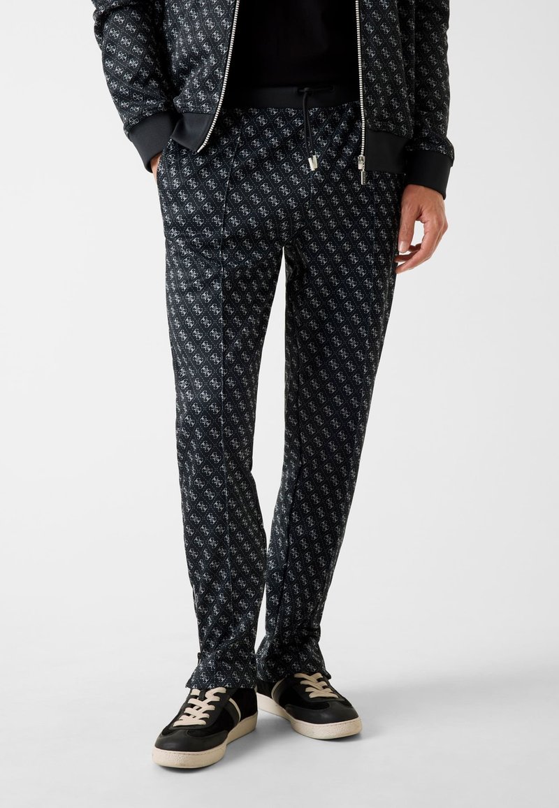 Marineblaue Jogginghosen mit Muster und Kordelzug am Bund, versehen mit einem dezenten durchgängigen Logodesign und Seitentaschen. Kombiniert mit schwarzen und beigen Sneakern.