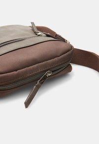 Brown zippered bag with a textured finish, featuring a darker top panel, an adjustable strap, and silver-tone hardware accents.