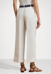 Wide-leg, ivory linen pants with visible side pockets and cuffed hems, paired with a navy woven belt. Brown strappy sandals visible.