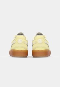 Gule mockaskinn sneakers med grå detaljer, med teksturerte gummisåler og en logo på bakhælen. Lavt snitt og snøring foran.