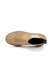 Zapato de ante marrón claro, tipo slip-on, con una puntera redondeada, paneles elásticos laterales y una pestaña en el talón de color negro. Textura suave con un brillo sutil.