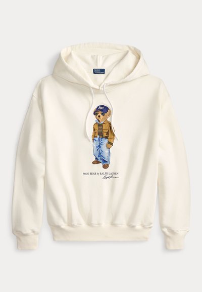 Λευκό φούτερ με κουκούλα με γραφικό Polo Bear που φοράει καφέ τζάκετ, μπλε τζιν και μπλε καπέλο, με κείμενο "Polo Bear by Ralph Lauren" από κάτω.