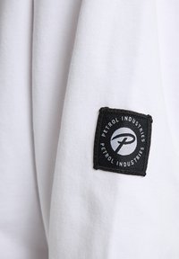 Tessuto bianco con una consistenza liscia, caratterizzato da un'etichetta rettangolare nera cucita sulla manica con il logo "Petrol Industries".