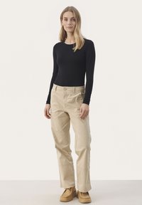 Svart långärmad skjorta i kombination med beige löst sittande byxor och bruna skor. Tyget är mjukt; byxorna har en knapp och fickor.