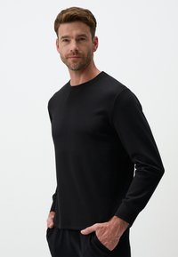 T-shirt nera a maniche lunghe in tessuto morbido con colletto rotondo, design aderente e polsini a coste. Pulita e semplice, senza motivi.