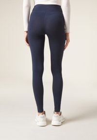 Marinblå leggings med hög midja, tajt passform och slät textur, i kombination med ljusa träningsskor.