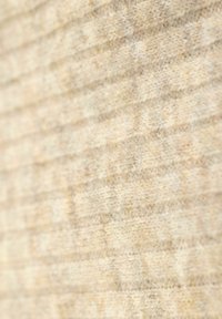 Tissu texturé dans des tons de beige, présentant un motif côtelé subtil et une texture douce et duveteuse, mettant en valeur sa construction tricotée et son aspect chaleureux.