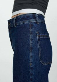 Vue latérale d'une personne portant un jean en denim bleu foncé taille haute et un top court noir et blanc.