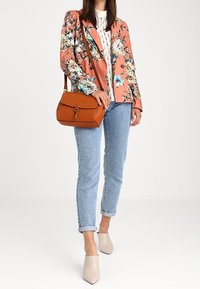 Blazer floreale rosa, camicetta bianca, jeans azzurri e mules beige. Borsa a tracolla marrone con patta e dettaglio decorativo in metallo.