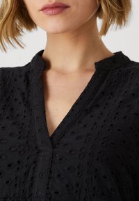 Top de algodón negro bordado con escote en V, que presenta detalles en ojal texturizados y una superficie sutilmente estampada.