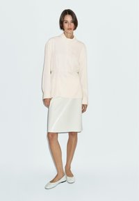 Haut rose clair à manches longues avec un col montant et une coupe décontractée, associé à une jupe crayon blanche. Des chaussures simples à semelle plate complètent l'ensemble.