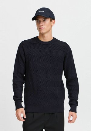 Suéter de punto azul marino con un patrón de espiga texturizado, cuello redondo y mangas largas. Combinado con un gorro a juego que presenta un texto.