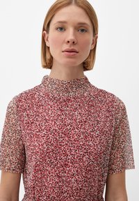 Vestido de flores rojas con cuello alto y mangas cortas. Tela transparente con un acabado ligeramente texturizado y cintura elástica.