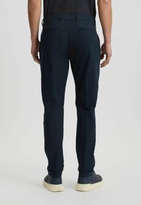 Dunkelblaue Hose im geraden Schnitt mit zwei Gesäßtaschen und glatter Textur. Kombiniert mit lässigen Schuhen.