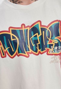 Balta medvilninė marškinėliai, papuošti spalvingu grafiti stiliaus tekstu mėlyna, raudona ir geltona spalvomis. Apima tekstą "KIEKVIENAM NEPAŽYSTAMAJAM" mažesniu šriftu.