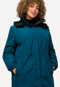 Tyrkysová vycpaná bunda s černým lesklým límcem, stahovaným pasem a bočními kapsami. Obsahuje pružné manžety a plný přední zip.