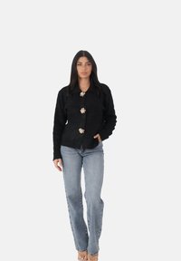 Cardigan nero realizzato in tessuto testurizzato, con chiusura a bottoni e tre bottoni a forma di fiore, abbinato a jeans a gamba dritta di un blu chiaro.