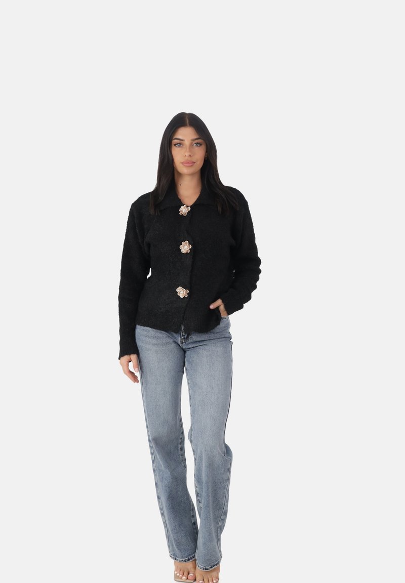 Cardigan nero realizzato in tessuto testurizzato, con chiusura a bottoni e tre bottoni a forma di fiore, abbinato a jeans a gamba dritta di un blu chiaro.