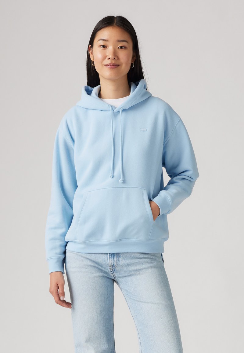 Hoodie azzurro chiaro con tasca a canguro, cappuccio con cordino regolabile e polsini a coste. Realizzato in morbido tessuto, abbinato a jeans di denim chiaro.