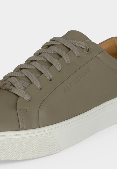 Baskets basses vert olive avec semelle épaisse en caoutchouc blanc et lacets assortis vert olive, avec nom de marque embossé sur le côté.