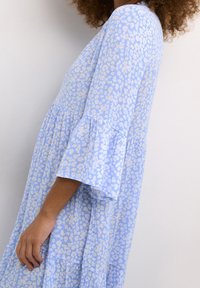 Světle modré šaty s květinovým vzorem, mají rozšířené rukávy a vrstvený lem. Vyrobeno z lehkého materiálu s mírně texturovaným povrchem.