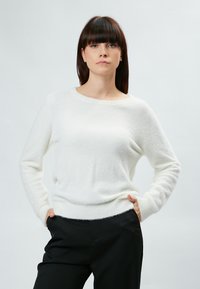 Maglione bianco e soffice con scollo rotondo e maniche lunghe, abbinato a pantaloni neri. Il capo ha una texture morbida e una vestibilità comoda.