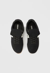 Μαύρα αθλητικά παπούτσια από σουέντ με υφή στον επάνω μέρος, σχέδιο με κορδόνια, επενδεδυμένο γιακά και λευκές λεπτομέρειες. Περιλαμβάνει εξωτερική σόλα από καουτσούκ χρώματος μουστάρδας.