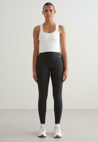 Valkoinen ribattu hihaton paita yhdistettynä mustiin ribattuihin legginsseihin. Legginsseissä on korkea vyötärö ja ne on tyylitelty valkoisten urheilujalkineiden kanssa.