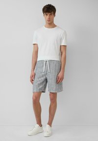 Witte t-shirt met korte mouwen, gedragen met blauw-witte gestreepte shorts met een elastische tailleband en trekkoord, aangevuld met witte sneakers.