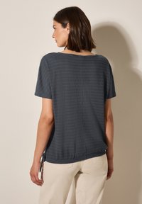 Haut gris foncé à manches courtes avec des rayures texturées, col rond et détail de lien sur le côté. Associe avec un pantalon de couleur claire.