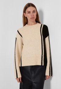 Beege värvi kudumisi sweater mustade vertikaalsete triipudega, laia soonikkoega äärisega ja pikkade varrukatega. Tekstuuriga kangas, mis on veidi vabalt istuv.