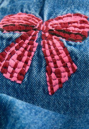 Material de denim brodat, prezentând o fundă mare roz cu detalii complexe țesute. Fundalul este o textură standard de denim albastru.
