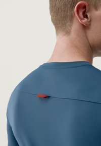 Modrá košile s krátkým rukávem, která se vyznačuje hladkým texturem, kulatým výstřihem a kontrastním červeným akcentem na zadní straně.