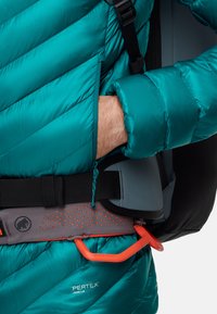 Teal isoleret jakke med quiltet mønster, der har et gråt bælte med orange detaljer og en karabiner til klatring eller fastgørelse af udstyr.