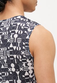 Ärmelloses, tailliertes Oberteil mit geometrischem Muster in Weiß und Marineblau, das verschiedene Formen und Texturen aufweist. Sichtbare Nähte an der Armausschnitt.
