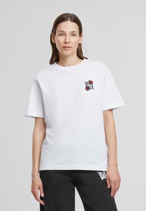 Witte katoen t-shirt met korte mouwen, voorzien van een zwart en rood geborduurd rozenlogo op de linkerkant van de borst. Relaxte pasvorm, ronde hals.
