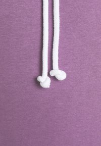 Fond en tissu violet avec deux cordons blancs suspendus, chacun se terminant par un nœud simple.