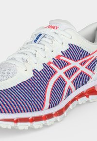 Λευκό παπούτσι τρεξίματος με μπλε και κόκκινο ριγέ μοτίβο, κόκκινο λογότυπο ASICS, λευκά κορδόνια και μαξιλαρωμένη κόκκινη και λευκή σόλα.