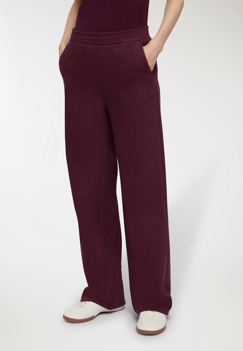 Bordowe dresy z szerokimi nogawkami, elastycznym pasem i kieszeniami bocznymi, wykonane z miękkiego materiału, w połączeniu z białymi trampkami.