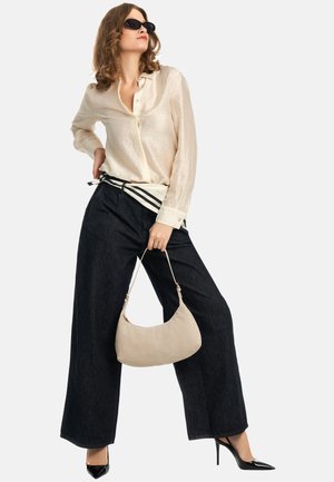 Jasnobeżowa koszula zapinana na guziki, szerokie ciemne spodnie jeansowe, czarne szpiczaste szpilki oraz miękka beżowa torebka o zaokrąglonym kształcie z paskiem.