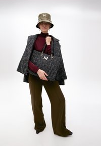 Černá a multikolorová tkaná taška s dvojitými černými uchy a bílým logem "M", v kombinaci s olivovou kloboukem typu bucket a strukturovaným kabátem.