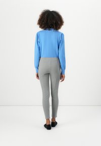 Blauwe langesleeve top met opgeblazen schouders, gecombineerd met strakke grijze leggings. Beide kledingstukken hebben een gladde textuur en een elegante uitstraling.