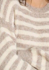Maglione a righe caratterizzato da una miscela di colori beige chiaro e crema con una texture morbida e pelosa. Le righe variano in larghezza e sono uniformemente distanziate.