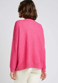 Pull en rose surdimensionné en maille douce, avec des épaules tombantes, des poignets côtelés et un ourlet asymétrique.