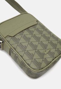Borsa a tracolla verde oliva realizzata in materiale sintetico testurizzato, caratterizzata da un motivo geometrico, pattina superiore e dettaglio del logo impresso.