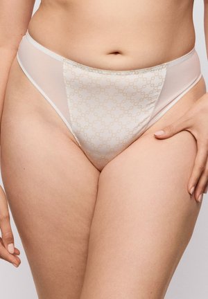 Vrouw draagt beige ondergoed met een hoge taille, voorzien van een subtiel schakelmotief en doorschijnende zijpanelen, hand rustend op de bovenkant van de dij.